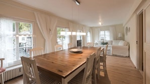 A spacious dining area with a wooden table and chairs, large windows with curtains, and a view of the outside.
