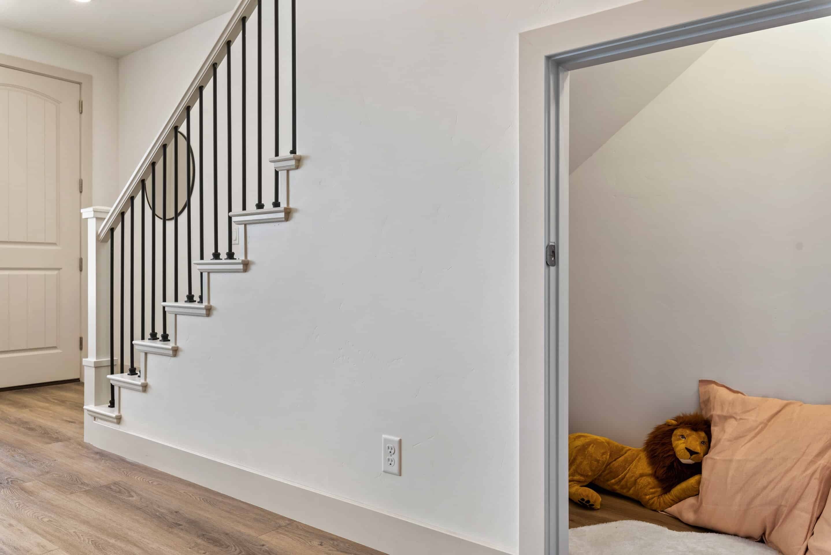 A staircase with a white wall and a plush toy lion on a bed.
