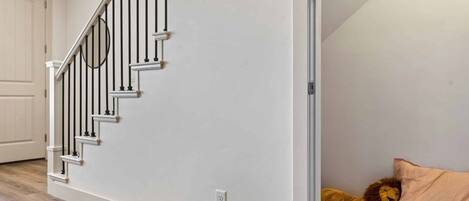 A staircase with a white wall and a plush toy lion on a bed.