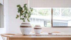 Ett matbord i trä med en flätad bänk, en hängande lampa och en krukväxt.