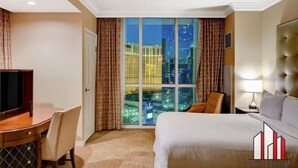 Ein Hotelzimmer mit großem Fenster, einem Bett, einem Schreibtisch mit Stuhl und einem Fernseher.