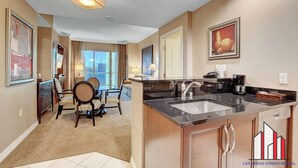 A modern kitchen with a large island, a dining area with a table and chairs, and a view of the city through large windows. - Signature 2Br3Ba F1 View Balcony Ste 30-719 and 21 (Las Vegas)