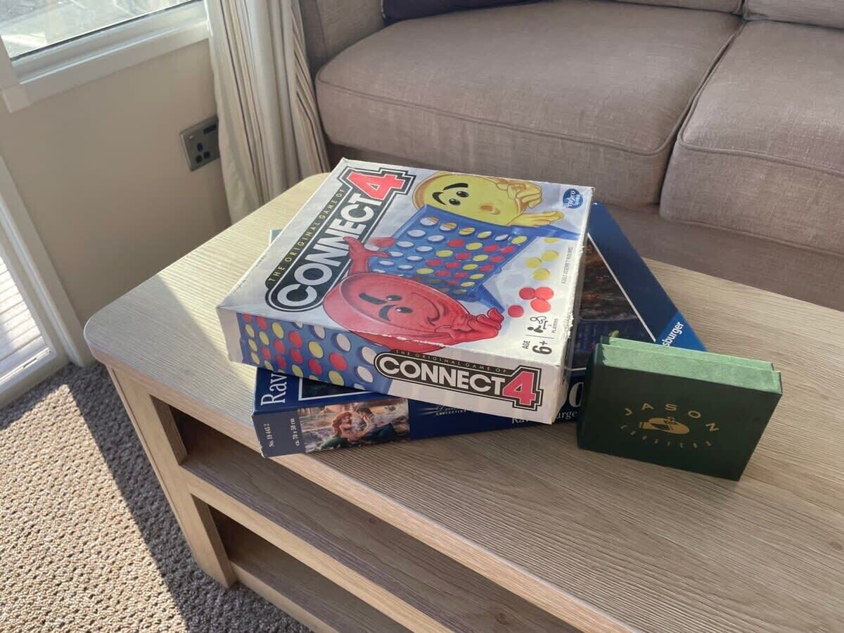 Eine Connect 4 Spielbox auf einem Holztisch, neben ihr ein grünes Buch.