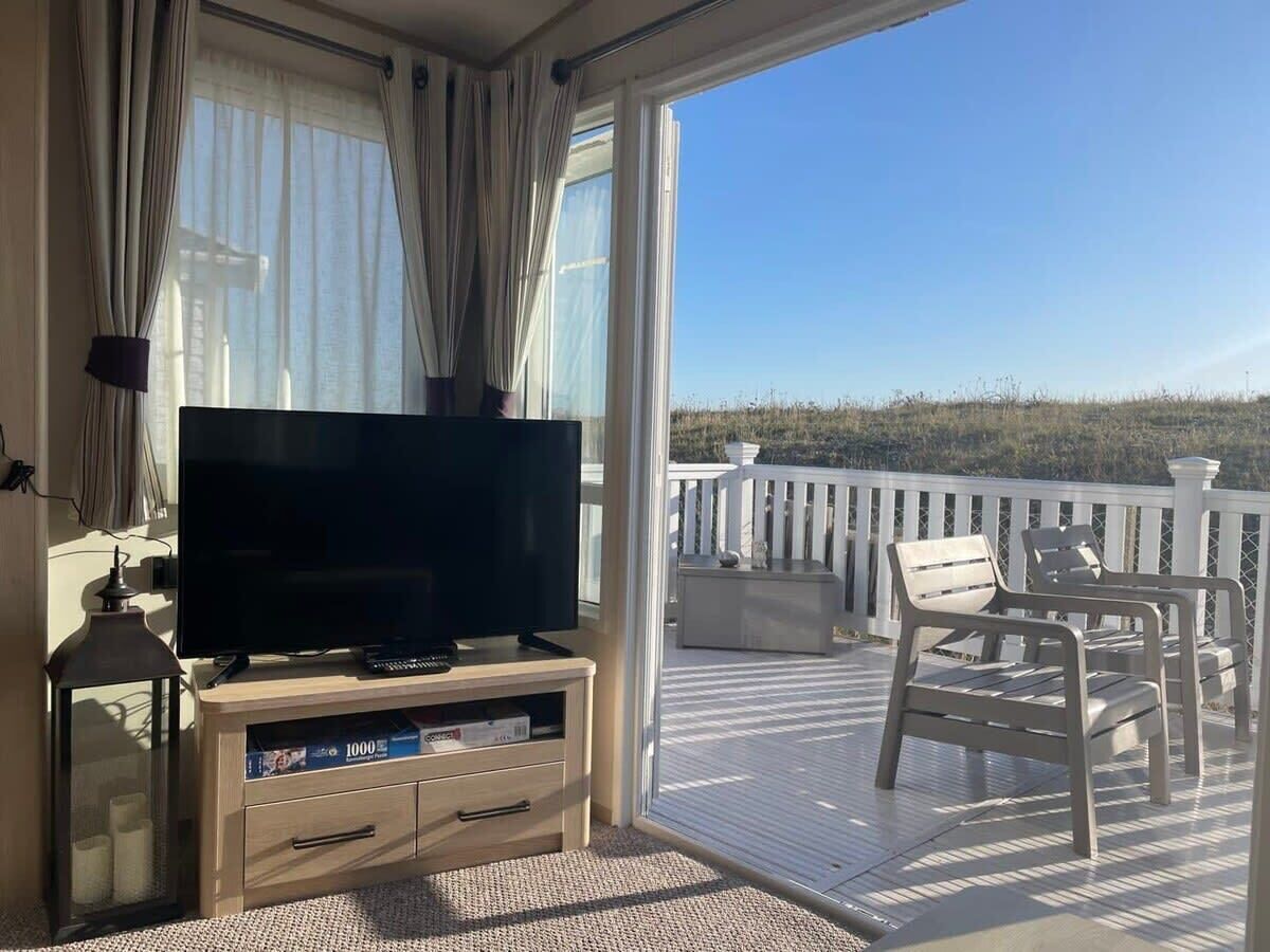 Un balcon avec un téléviseur posé sur un meuble en bois, des meubles d’extérieur blancs et une vue sur le paysage.