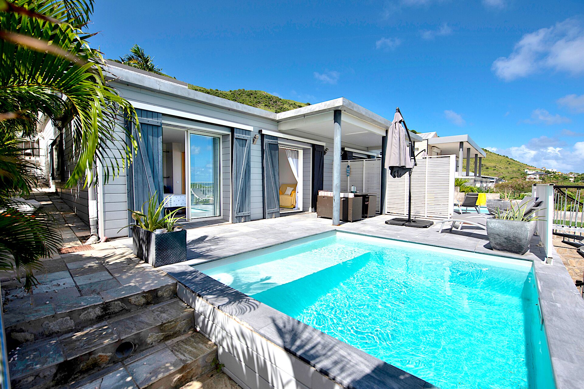 A modern pool area with a clear blue pool, a covered seating area, and a view of a hillside.