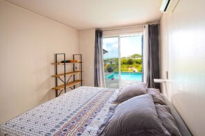 A bedroom with a bed, a wooden shelf, and a view of a swimming pool.