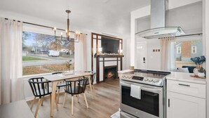 Et moderne køkken med stor komfur, pejs og spiseplads med træstole og bord.