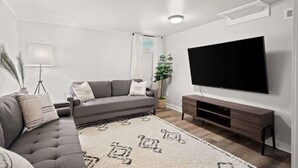 En moderne stue med en grå sofa, et fladskærms-tv monteret på væggen, et træunderholdningsmøbel og et mønstret tæppe.