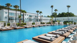 A poolside area with lounge chairs and a modern building in the background. - So White Beach Resort (Ayia Napa)