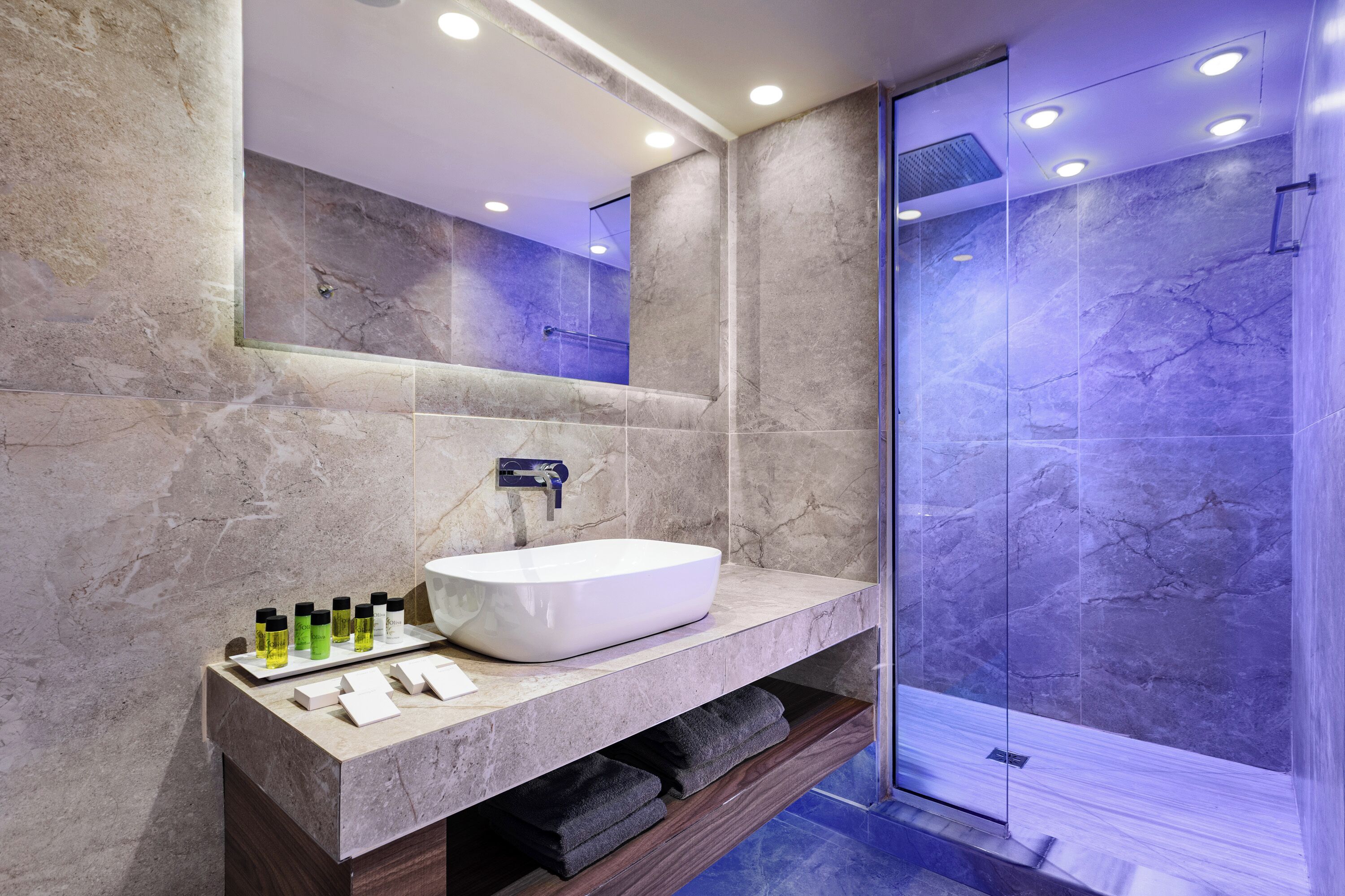 A modern bathroom with a large mirror, a white vessel sink, and a glass-enclosed shower.