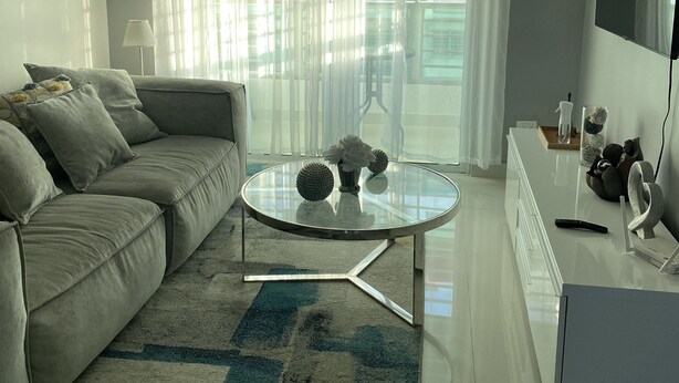 A modern living room with a sofa, a glass coffee table, and a TV on a stand. - Beautiful apartment in residential in front of the sea (Santo Domingo Este)