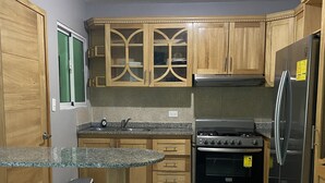 A kitchen with wooden cabinets, a granite countertop, a stainless steel refrigerator, and a gas stove. - Beautiful apartment in residential in front of the sea (Santo Domingo Este)