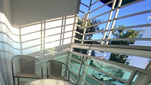 A balcony with a glass table and chairs, large windows, and a view of parked cars and greenery. - Beautiful apartment in residential in front of the sea (Santo Domingo Este)