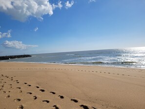 Une plage où l’on peut voir des empreintes de pas menant à l’eau, un brise-lames rocheux et un ciel dégagé.