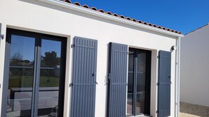 Ein modernes Gebäude mit großen Glasfenstern und Rollläden, einem Ziegeldach und blauem Himmel.