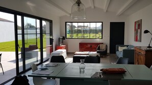 Ein modernes Wohnzimmer mit einem großen Glasfenster zum Patio, einem Kamin und Blick auf eine grüne Landschaft.