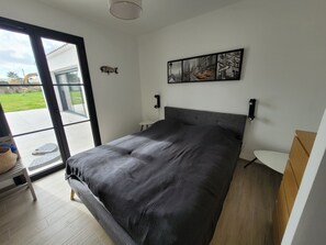 Une chambre moderne avec un grand lit, une porte-fenêtre coulissante donnant sur un balcon et un tableau représentant un paysage urbain accroché au mur.