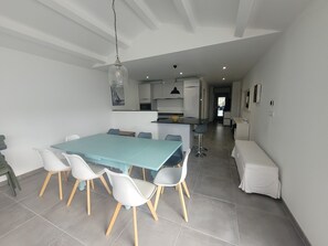 Une cuisine moderne avec des meubles blancs, un îlot central et un coin repas comprenant une table de couleur turquoise et des chaises blanches.