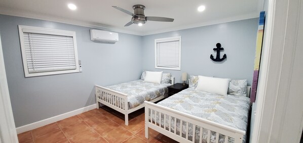 A bedroom with two beds, a ceiling fan, and an air conditioning unit.