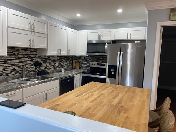 A modern kitchen with white cabinets, a wooden island, stainless steel appliances, and a tiled backsplash. - Beautiful, Cozy Beach Villa In The Heart Of Treasure Cay! (Treasure Cay)