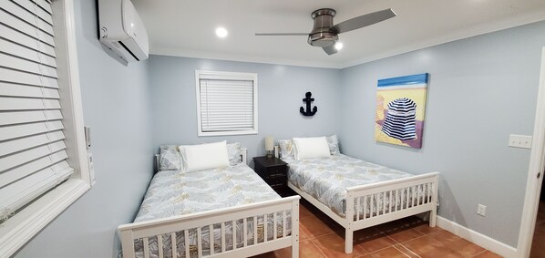 A bedroom with two beds, a ceiling fan, a window with blinds, a nightstand, and a wall-mounted anchor. - Beautiful, Cozy Beach Villa In The Heart Of Treasure Cay! (Treasure Cay)