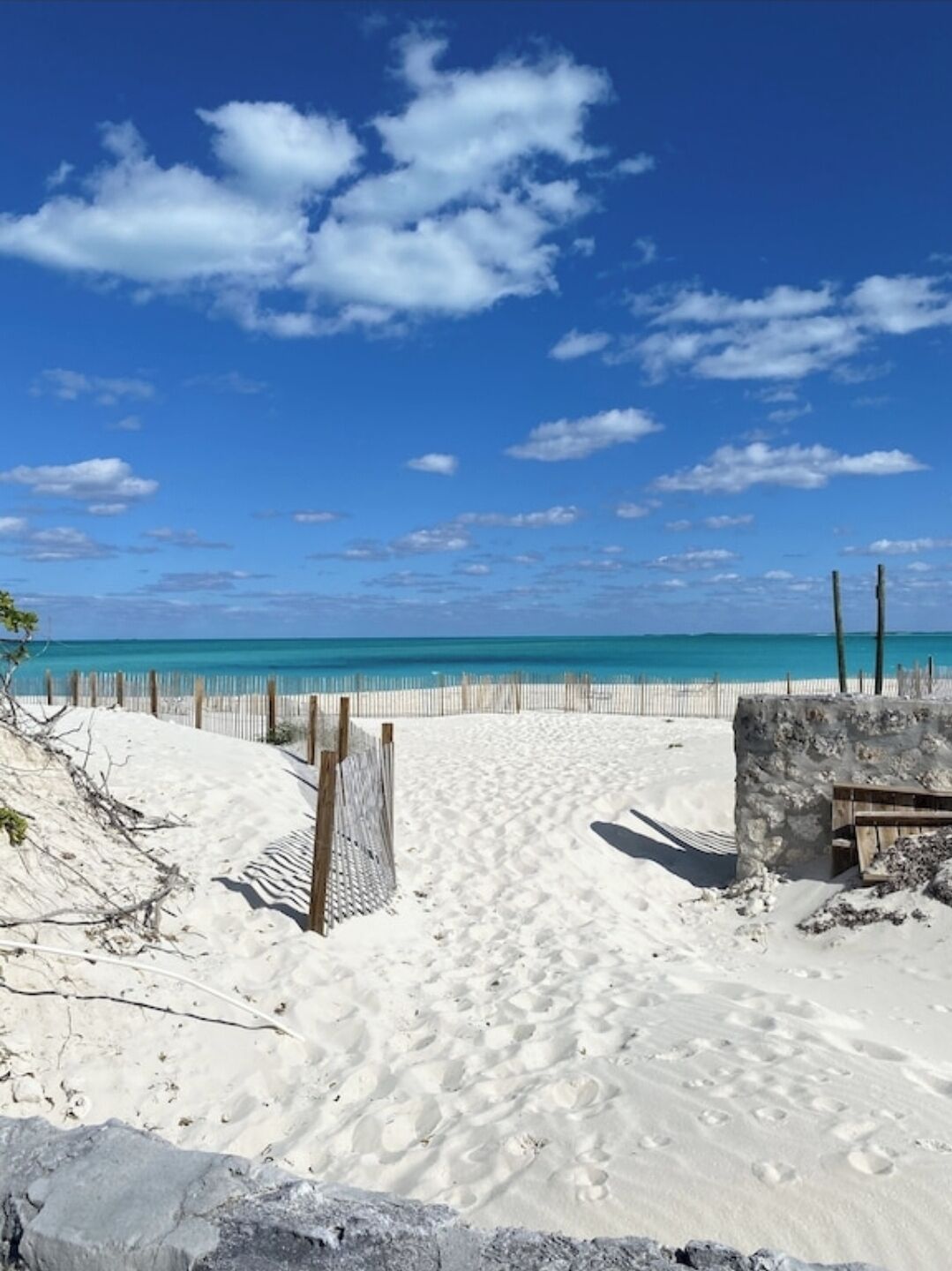 A sandy beach with a wooden fence and a stone wall, leading to the ocean.