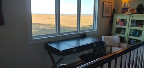 Una habitación con escritorio y silla, una ventana con vista a un campo, y un armario verde con objetos decorativos.