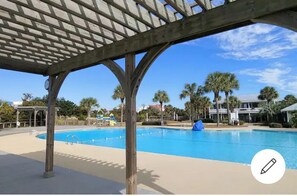 Zona de piscina con una pérgola de madera, palmeras y un cielo azul despejado.