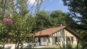 Une maison traditionnelle avec un toit en tuiles, entourée d’une végétation luxuriante et d’arbres.