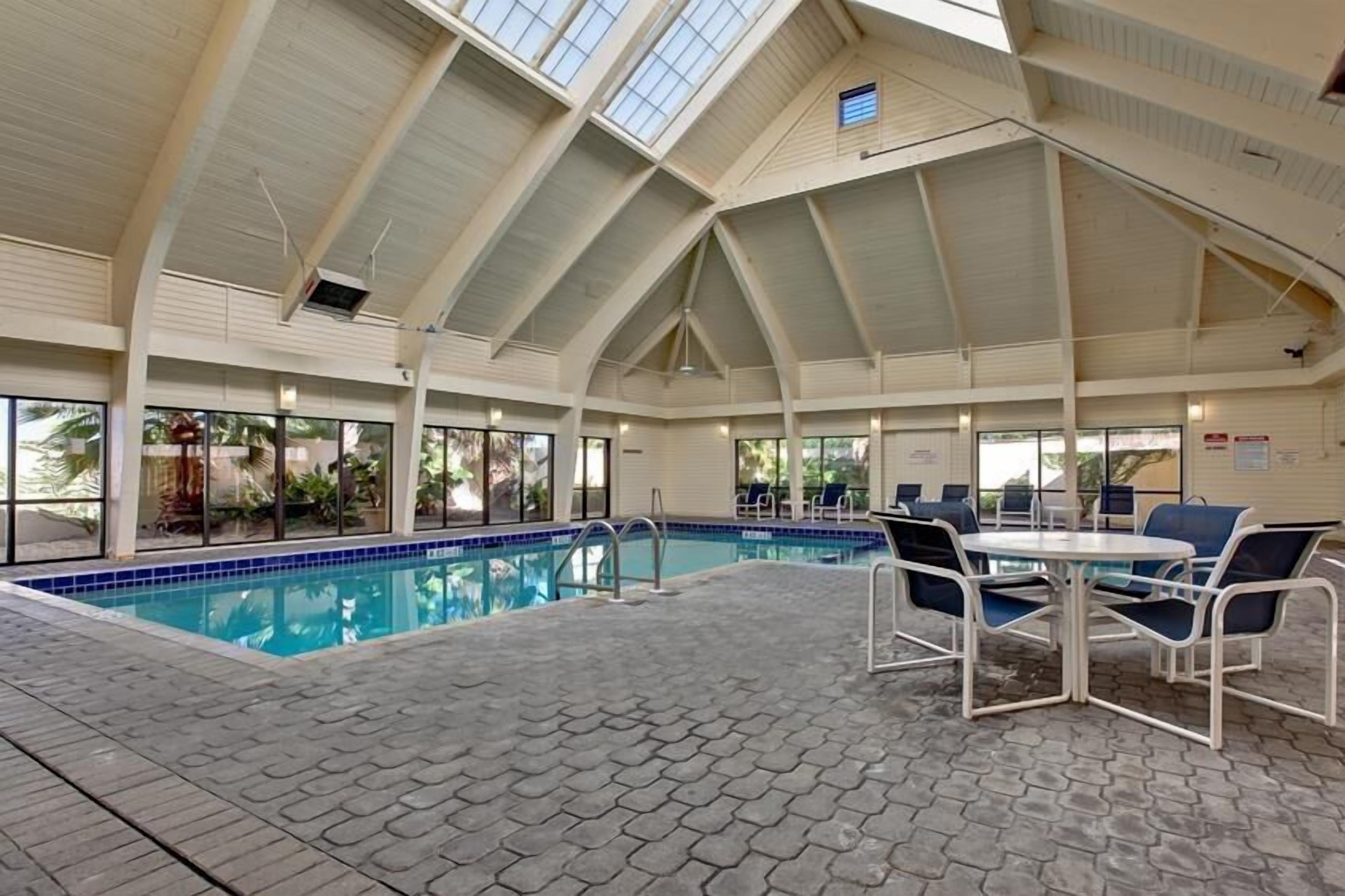 An indoor swimming pool with a tiled floor, surrounded by lounge chairs and a table.