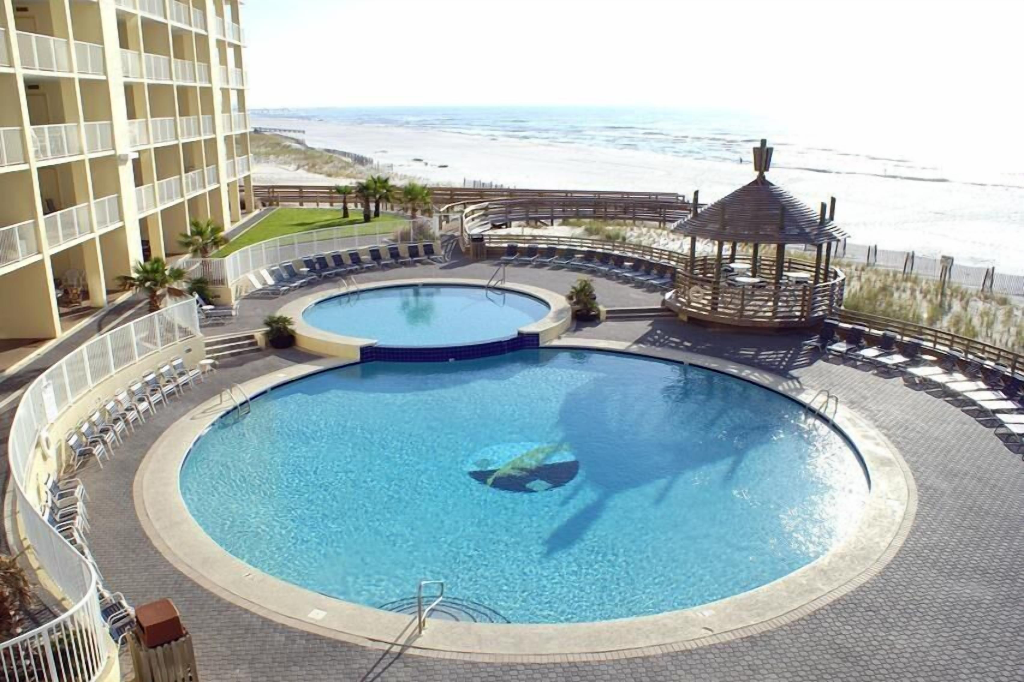Una piscina circular con un mirador, sillas de descanso y vistas a la playa.