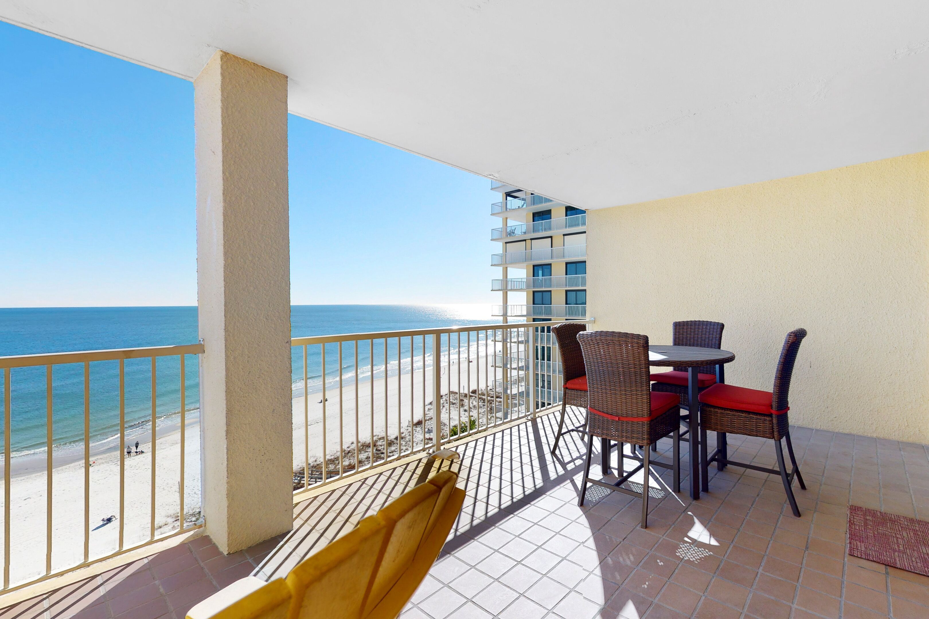 Un balcon avec vue sur la plage, une table avec des chaises et une chaise jaune.