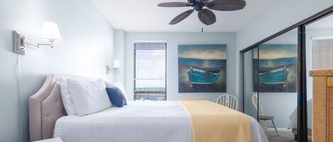 Un dormitorio con cama, ventilador de techo, ventana con persianas y dos cuadros en la pared.