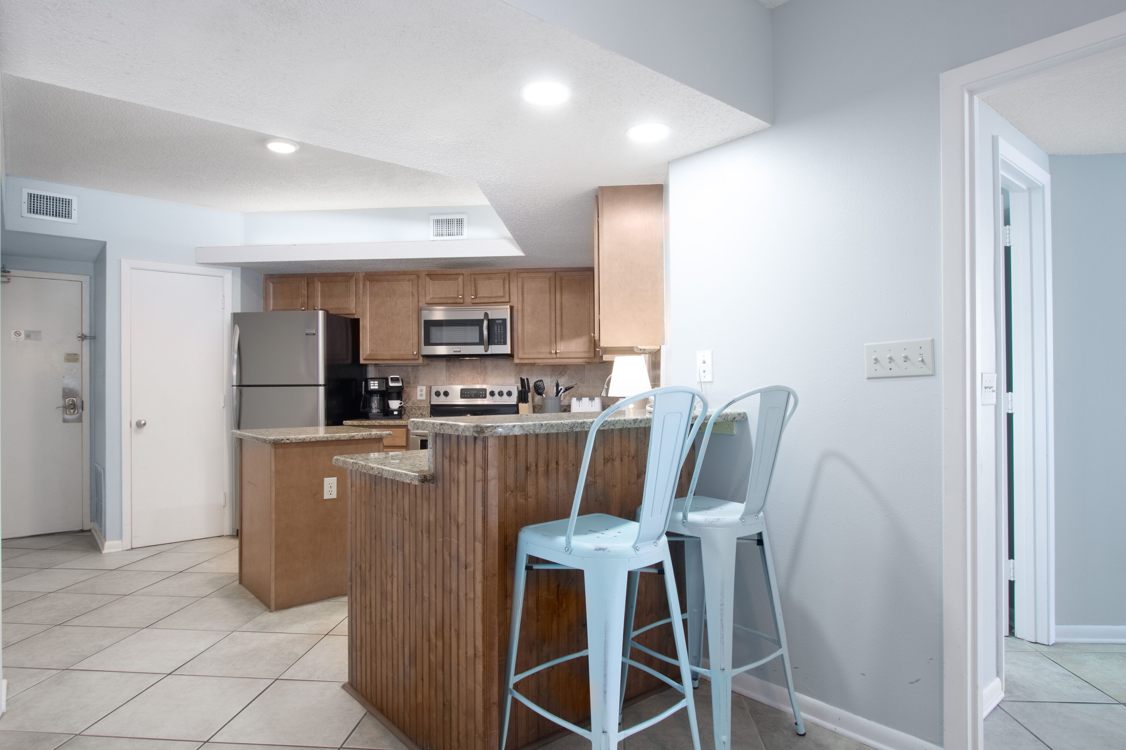 Una cocina moderna con armarios de madera, un refrigerador de acero inoxidable, un microondas y una barra con dos taburetes.