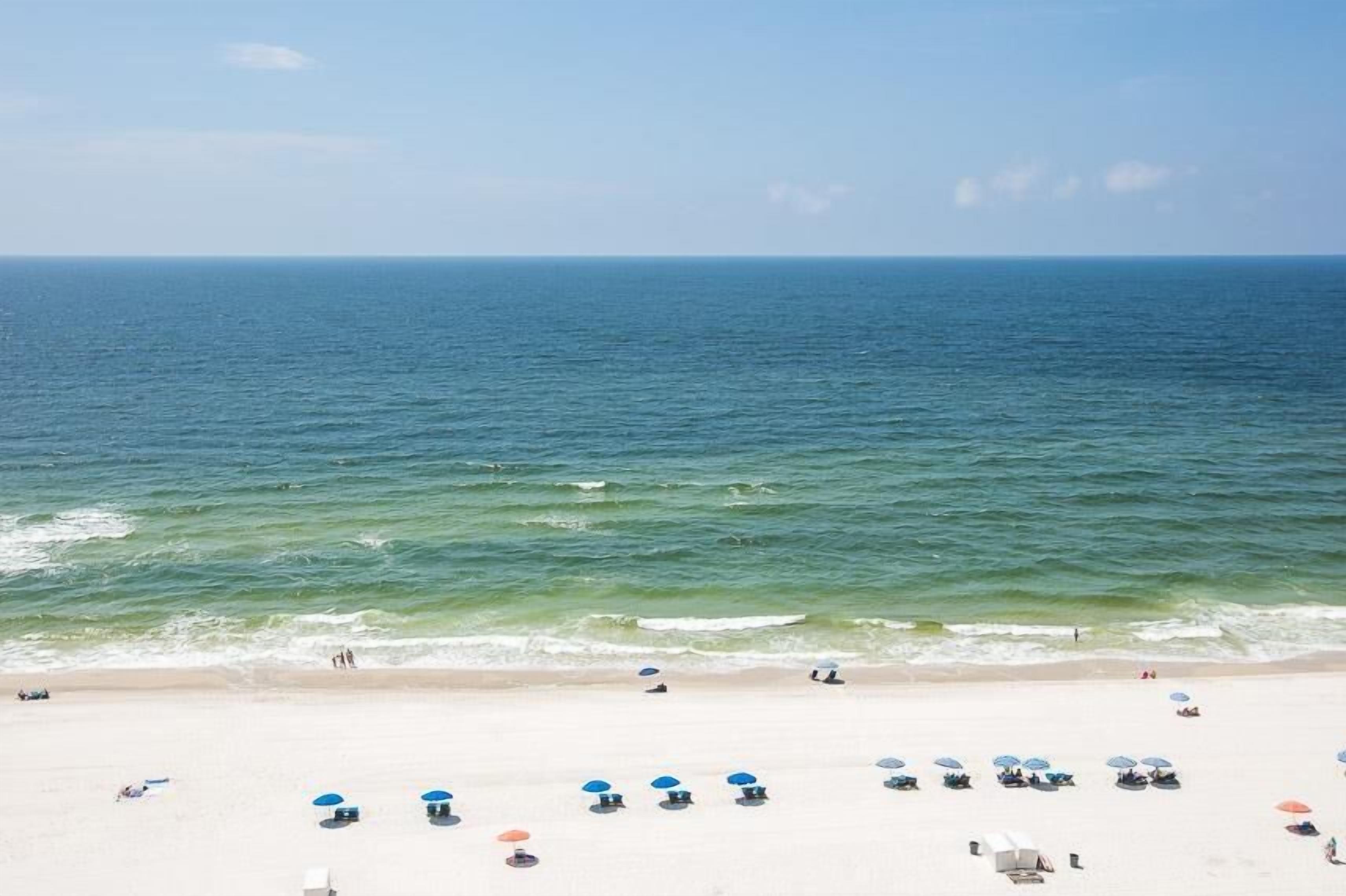 A beach with clear blue water, white sand, and several umbrellas.