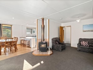 A living room with a fireplace, a dining area with wooden furniture, and a kitchen in the background. - Holiday Heaven - Cromwell (Cromwell)