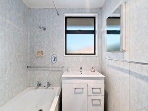 A modern bathroom with a bathtub, a sink, and a window providing a view of the sky. - Holiday Heaven - Cromwell (Cromwell)