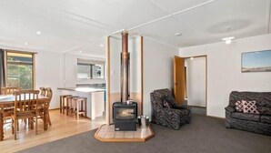 A modern living room with a wood-burning stove, a dining area with wooden chairs, and a sofa.