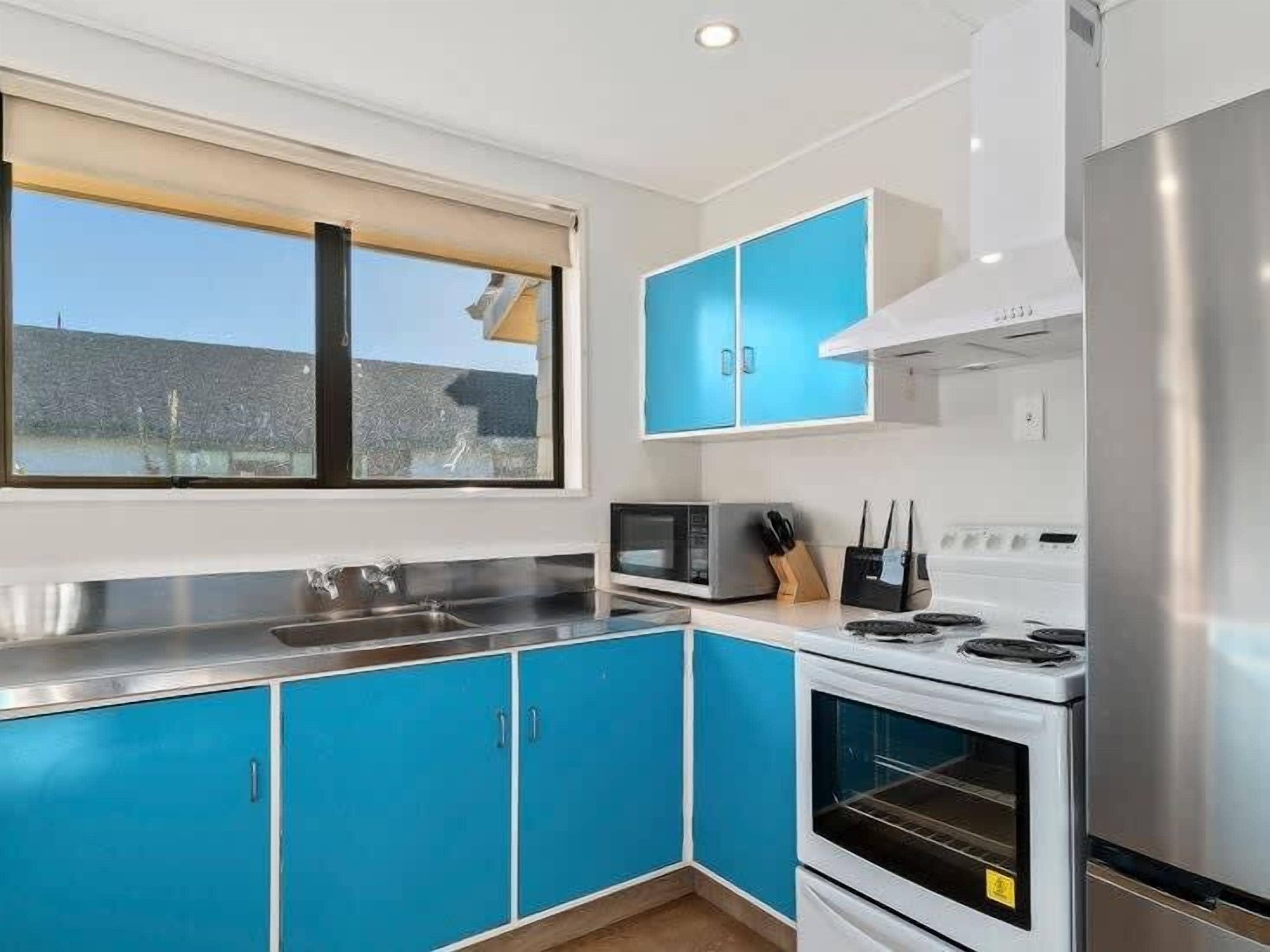 A modern kitchen with blue cabinets, stainless steel appliances, and a window providing a view.