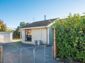 A single-story house with a garage, a fenced driveway, and a bush in the foreground.
