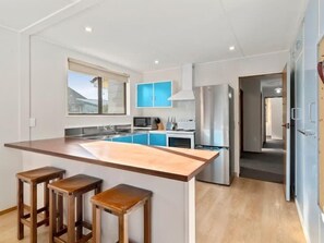 A modern kitchen with a central island, bar stools, a microwave, and a stainless steel refrigerator. - Holiday Heaven - Cromwell (Cromwell)