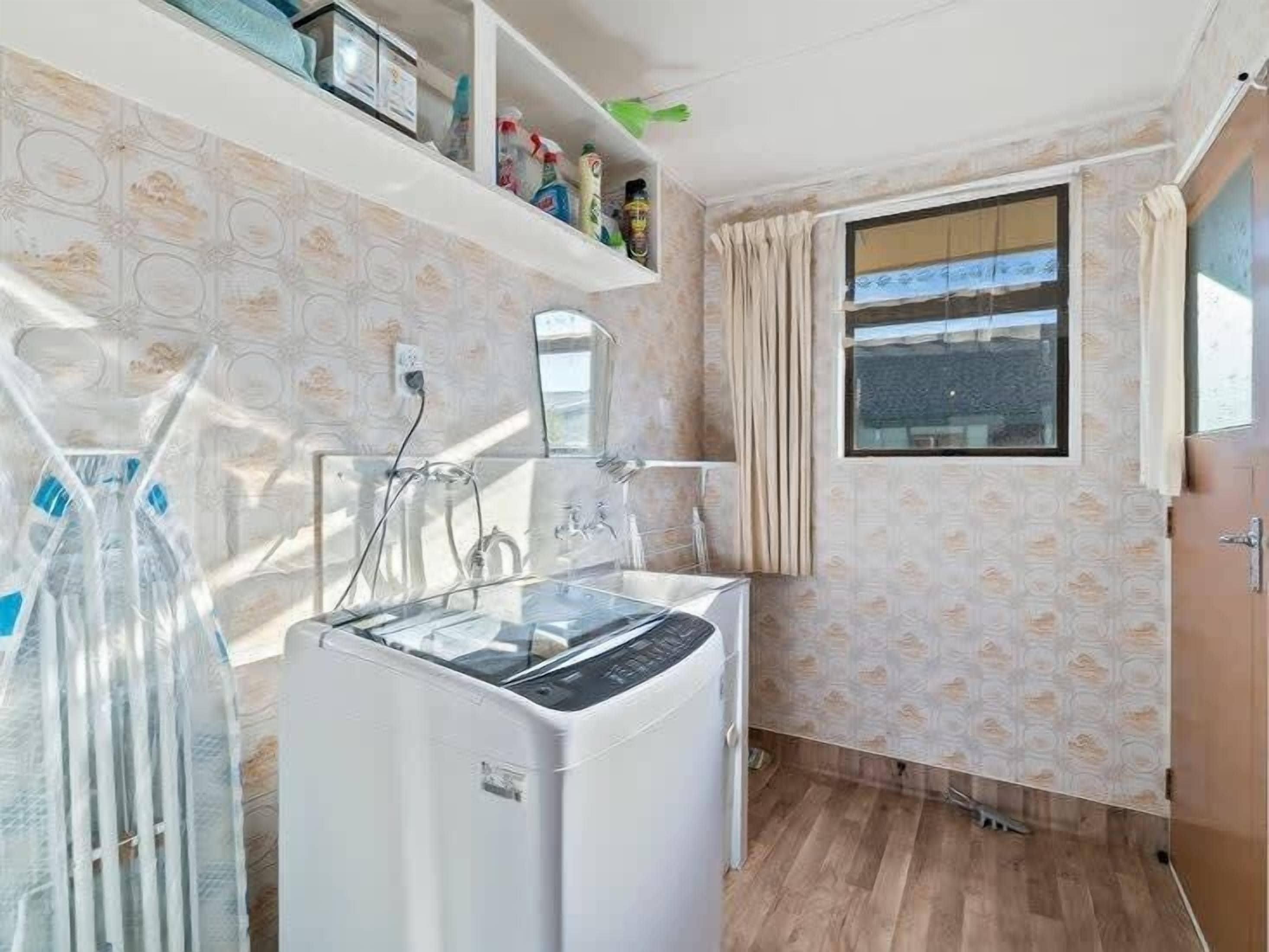 Un lavadero pequeño con lavadora, tendedero y ventana con cortinas.