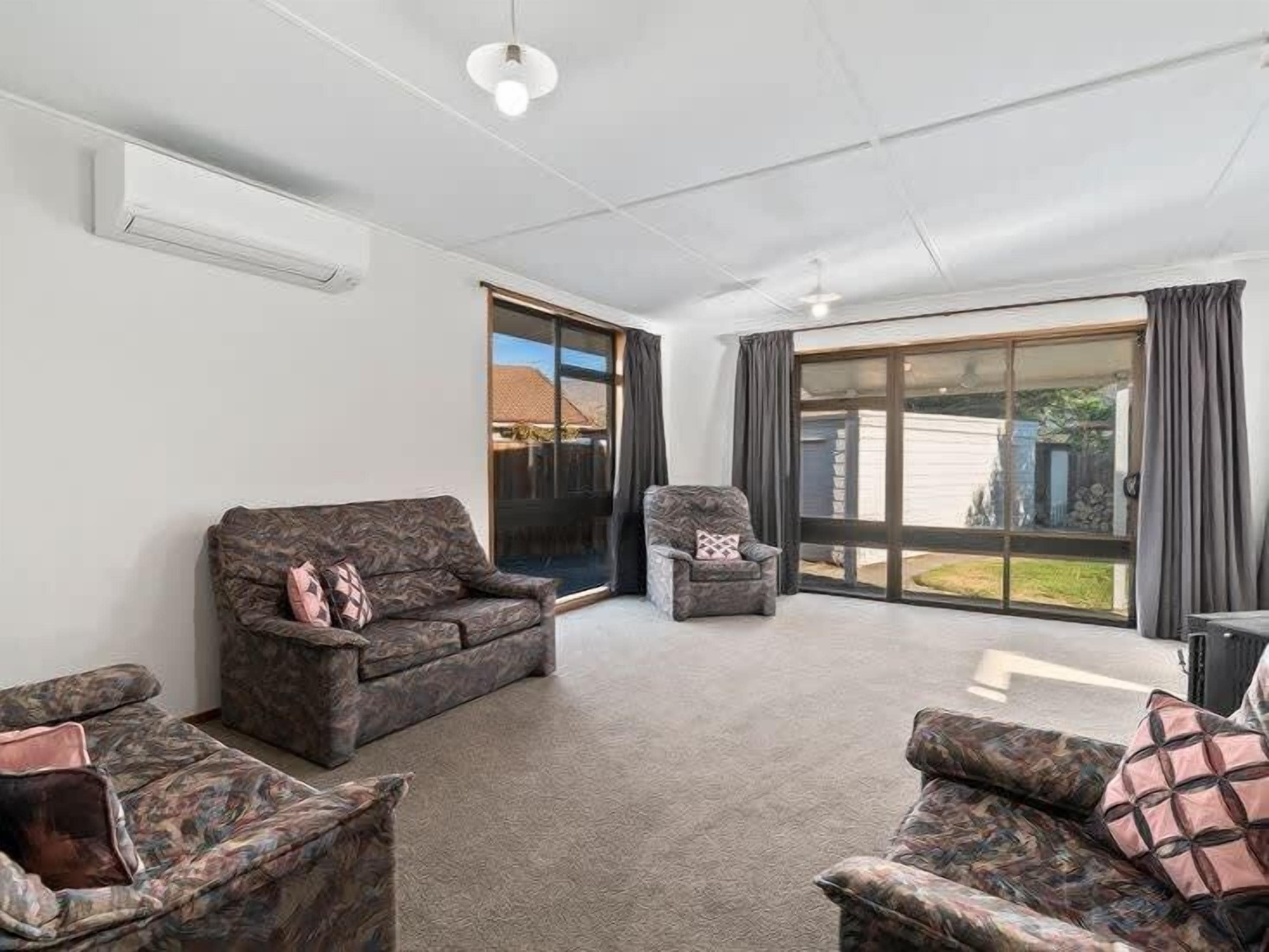 A spacious living room with a large sliding glass door leading to a backyard. There are two sofas and a chair.