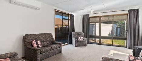 A spacious living room with a large sliding glass door leading to a backyard. There are two sofas and a chair.