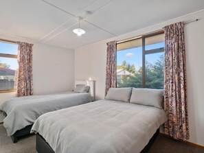 A room with two beds, a ceiling fan, and a window with curtains. - Holiday Heaven - Cromwell (Cromwell)