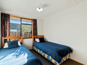 A room with two single beds, a window with curtains, and a ceiling light. - Holiday Heaven - Cromwell (Cromwell)