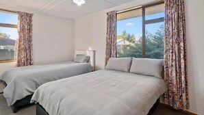 A room with two beds, a ceiling fan, and a window with curtains.