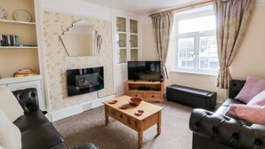 A living room with a television, leather sofas, a wooden coffee table, and a fireplace. - The Vale (Beaworthy)