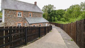 A stone house with a wooden fence and a paved path. - The Vale (Beaworthy)