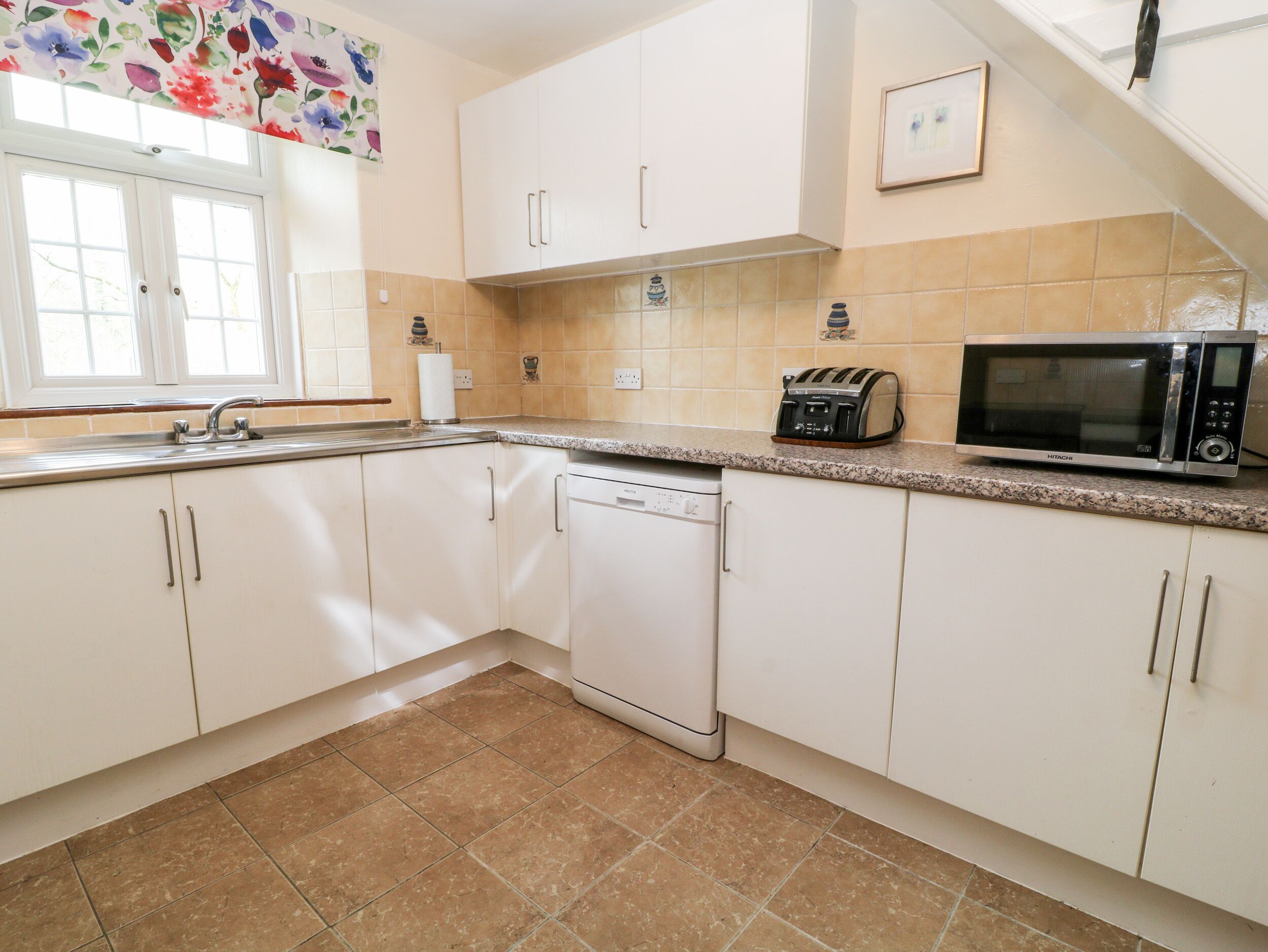 A kitchen with white cabinets, a dishwasher, a microwave, and a window with a floral curtain.
